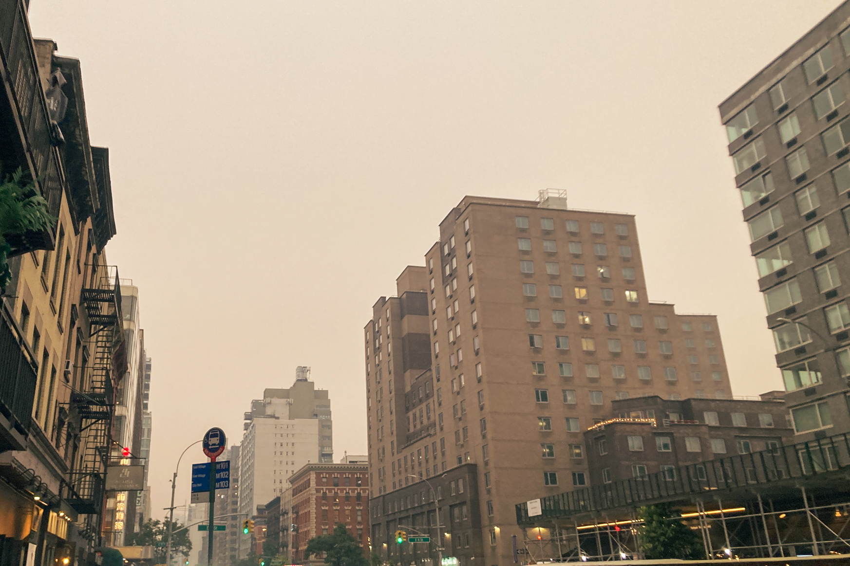 A photograph of a New York City block taken from street level. An ominous smoke turns the sky beige, as was the case throughout much of June 2023 due to Canadian forest fires.